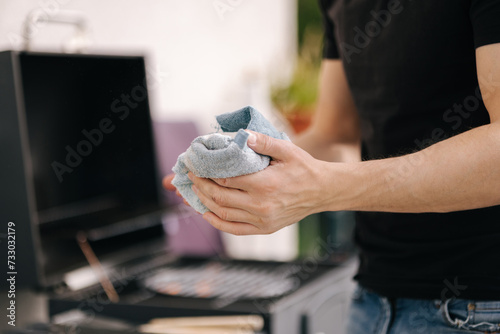 Close-up of male using towel to wipe dirt from hands while the fire is burning in the grill