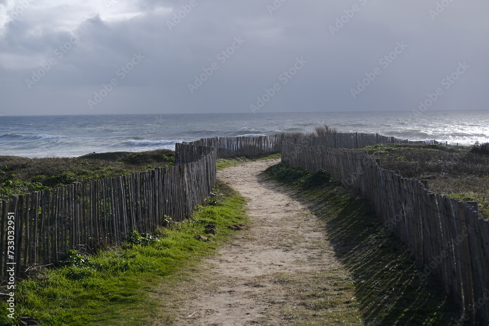 A small path through some wooden fence to reach the shore on a stormy day. Batz-sur-Mer, France - February 10, 2024.