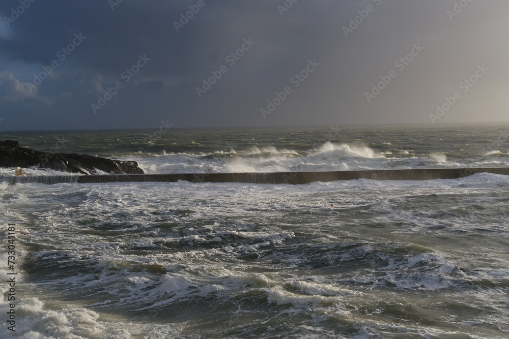 A view of the jetty of a small French harbor on a stormy day. Batz-sur-Mer, France - February 10, 2024.