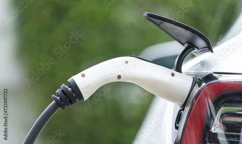 Closeup EV charger plug handle attached to electric vehicle port, recharging battery from charging station. Modern designed EV car and clean energy sustainability for better future.Panorama Synchronos © Summit Art Creations