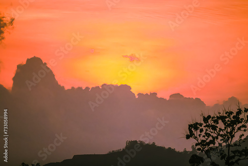 Top view of the sunset is getting disappearing in the sky. Clouds are orange yellow and pink with colorfull. There are many layers of mountains below. The idea for natural wallpaper with copy space. © Pang wrp