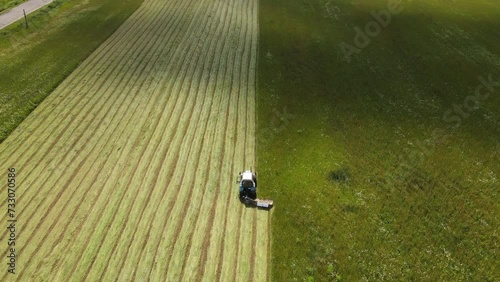 A tractor performs agricultural work on a green field covered with grass on a clear summer day, filmed from a drone