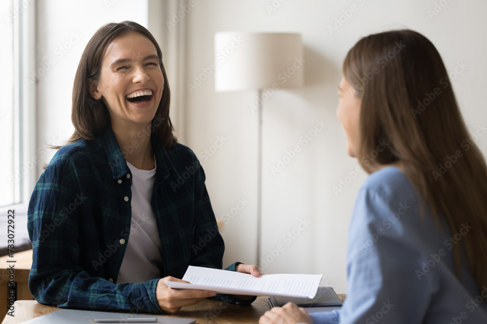 Cheerful project manager girl talking to business colleague in casual clothes, laughing, having fun, enjoying informal communication in office, holding work documents, sitting at workplace Cheerful project manager girl talking to business colleague in casual clothes, laughing, having fun, enjoying informal communication in office, holding work documents, sitting at workplace