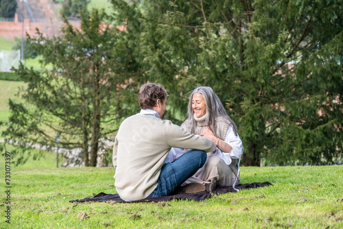 A man and a woman practising concentration exercises and spiritual connection sitting in a green meadow surrounded by trees in a park. © MelisaCabal