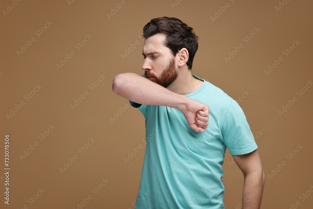 Sick man coughing into his elbow on brown background. Cold symptoms Sick man coughing into his elbow on brown background. Cold symptoms
