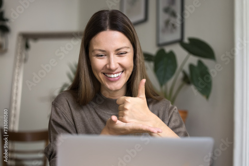 Cheerful hearing disability therapist talking on video conference call at laptop, speaking to patient, student, showing thumb up hand gesture on palm, smiling, laughing, enjoying communication photo