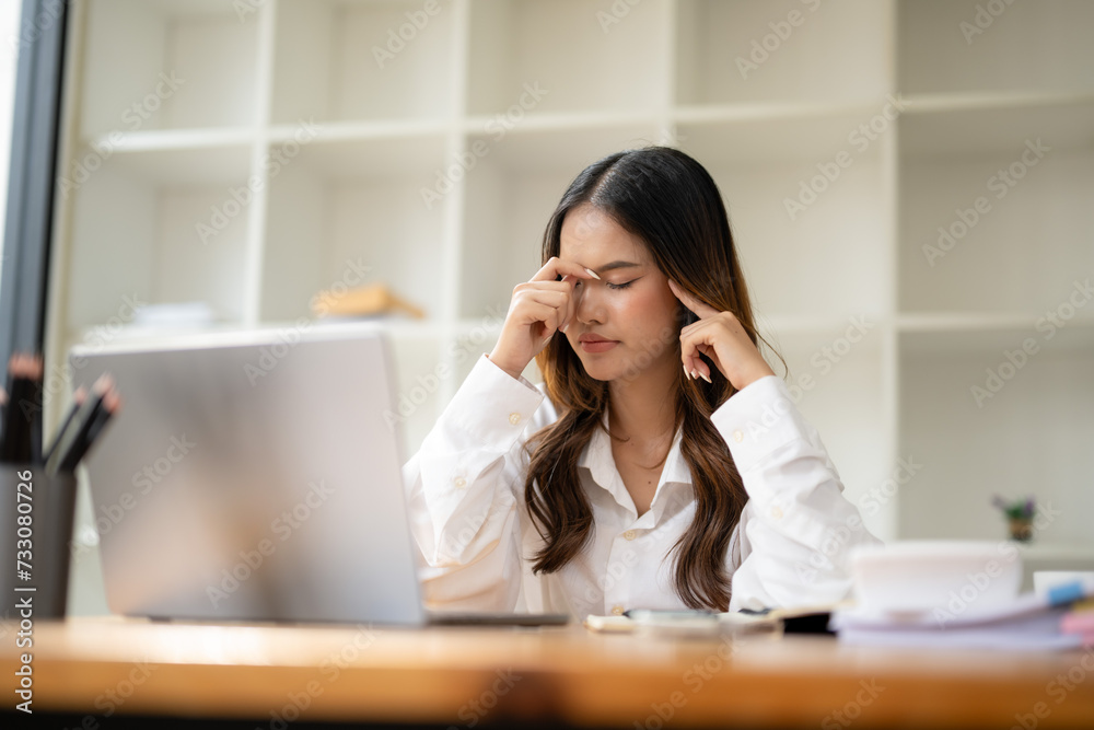 Focused businesswoman feeling a headache, massaging temples while working on a computer in a modern office..