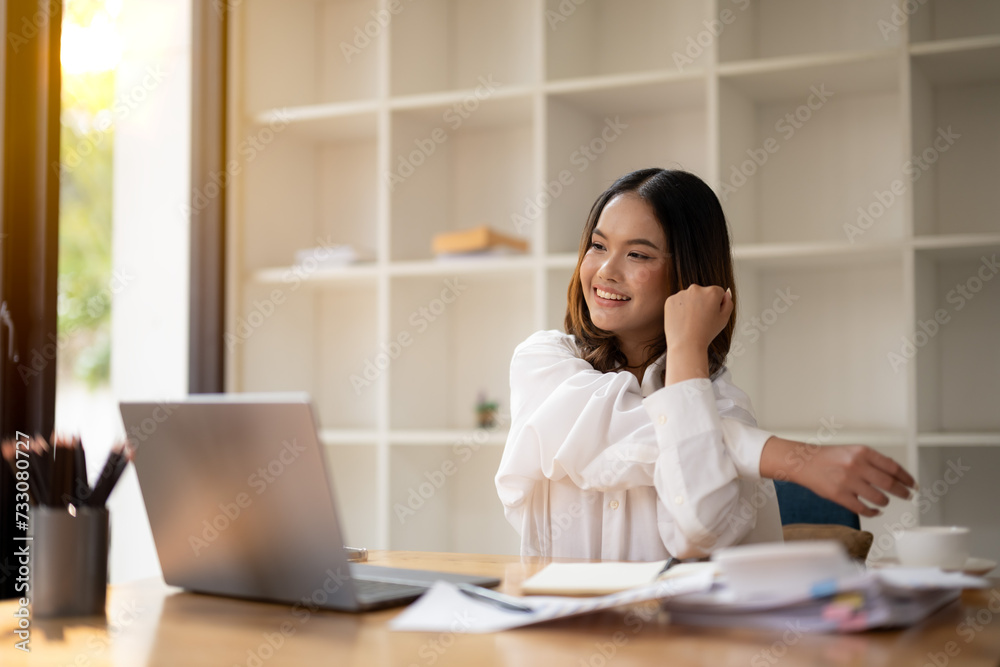 Young professional woman taking a stretching break at her office workspace, smiling with satisfaction. Young professional woman taking a stretching break at her office workspace, smiling with satisfaction.