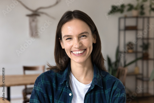 Happy attractive young woman in casual cloth posing in office, co-working apartment, looking at camera with toothy smile. Cheerful female freelancer, entrepreneur, student head shot portrait