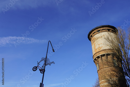 Looking up to limestone tower towards blue sky. Tree branches on the right. Street lamp with bicycle figure. Tallinn, Estonia, Europe. February 2024 photo