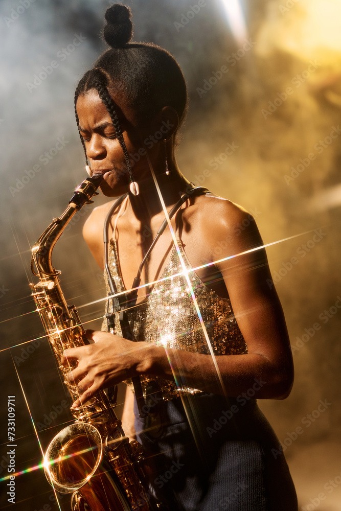 Vertical portrait of talented young woman playing saxophone during jazz music concert with golden light accents