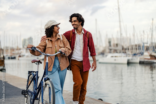 A happy trendy couple is taking a casual walk on the dock with bicycle.
