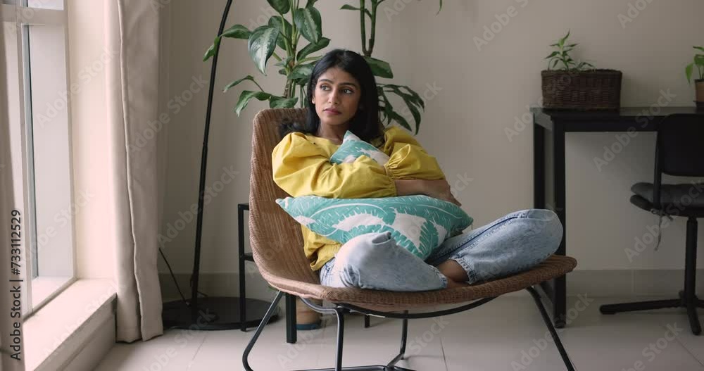 Indian woman looks frustrated or offended cuddling cushion sit in armchair, deep in sad thoughts, missing, waiting, feels bored on a day off at home alone. Loneliness, break up, after quarrel emotions