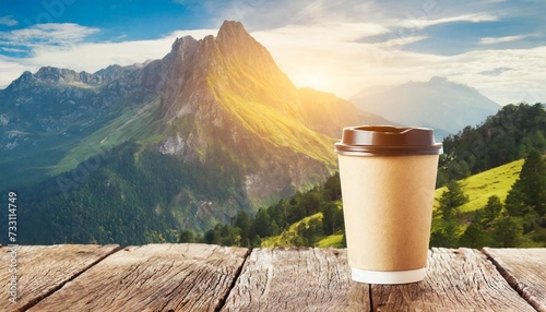 a paper coffee cup on wooden table and outdoor mountain and sunl photo