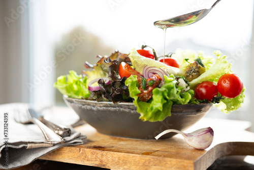 Colorful salad with fresh ingredients prepared with a spoon of olive oil in a ceramic bowl. Healthy nutrion concept for fitness and spring diet.  photo