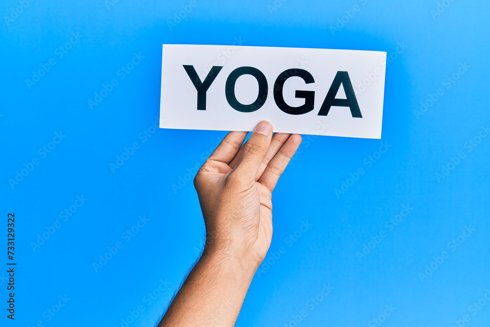 Hand of caucasian man holding paper with yoga word over isolated blue background Hand of caucasian man holding paper with yoga word over isolated blue background