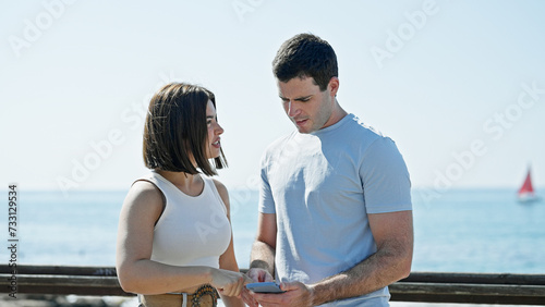 Beautiful couple using smartphone standing together at seaside