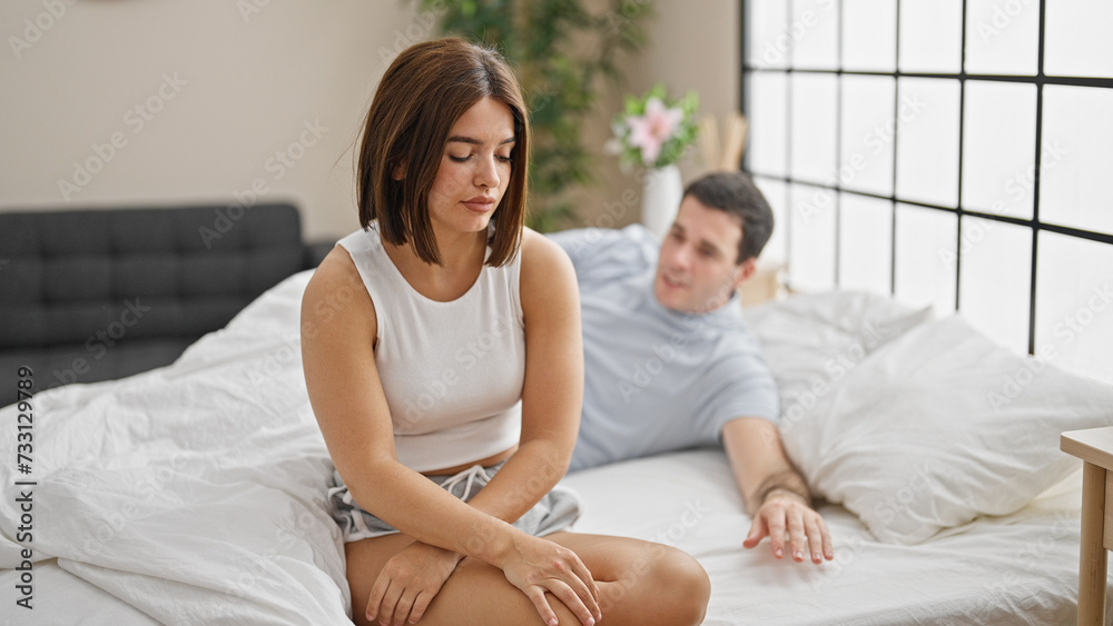 Beautiful couple sitting on bed with serious expression at bedroom Beautiful couple sitting on bed with serious expression at bedroom