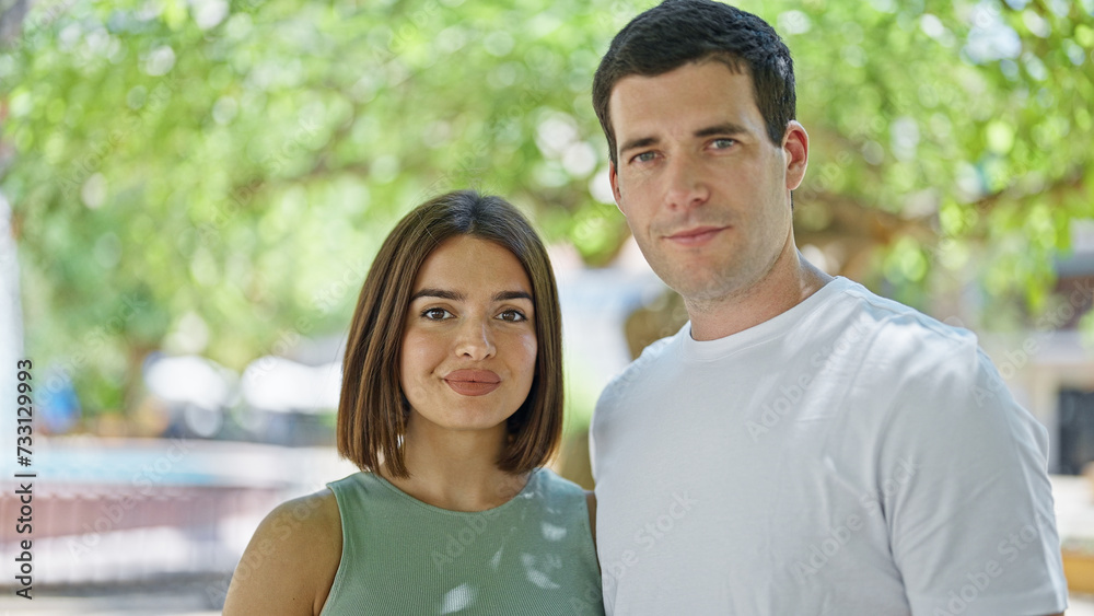 Beautiful couple standing together with serious face at park Beautiful couple standing together with serious face at park