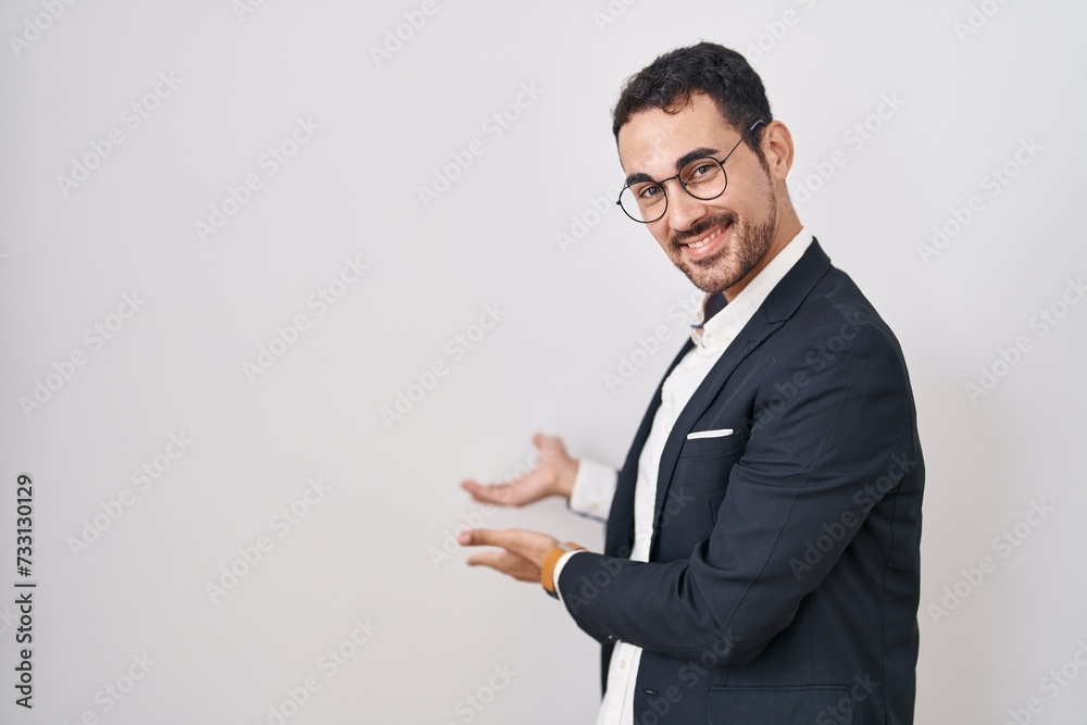 Handsome business hispanic man standing over white background inviting to enter smiling natural with open hand Handsome business hispanic man standing over white background inviting to enter smiling natural with open hand