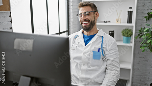 Confident young hispanic man working as a doctor at the clinic, smiling behind the computer
