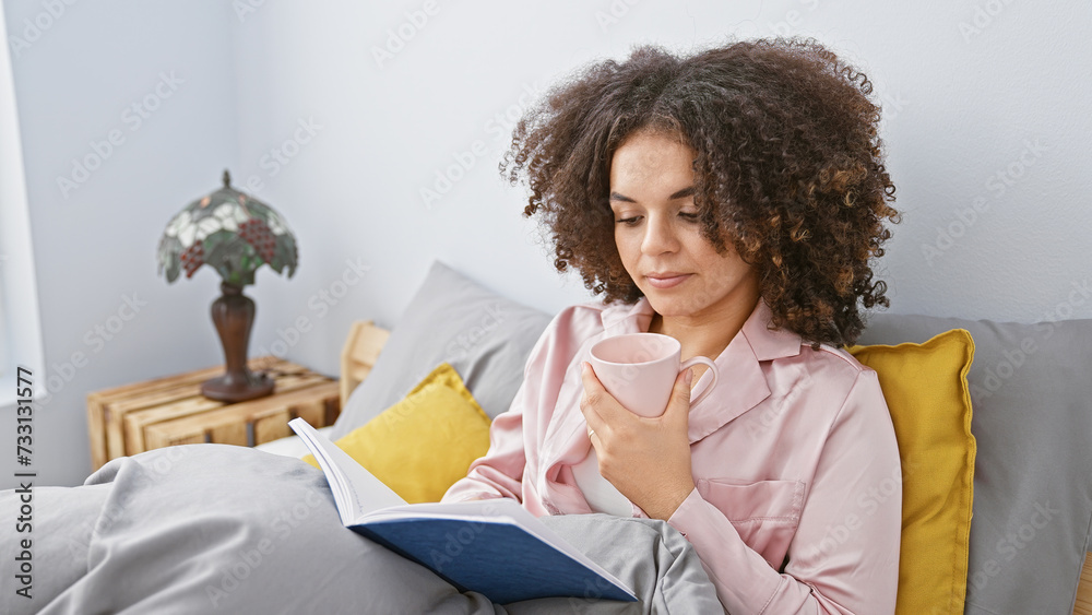 Young hispanic woman with curly hair, reading a book and enjoying coffee in a cozy home bedroom setting. Young hispanic woman with curly hair, reading a book and enjoying coffee in a cozy home bedroom setting.