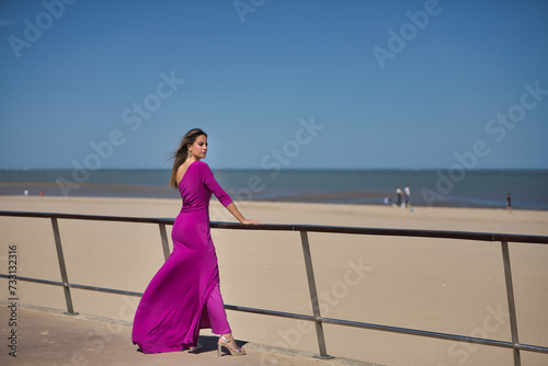 Young and beautiful woman in a purple dress and heels  leaning on a railing  posing while the air moves her hair and dress  by the sea. Concept beauty  fashion  trend.