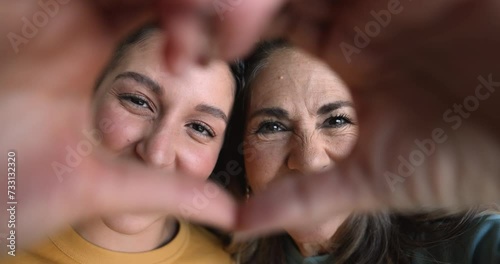 Close up faces of two Hispanic women, loving mature mum and grown up daughter showing heart symbol with joined fingers at camera. I Love You, Happy Mother's Day celebration, family unity and bonding
