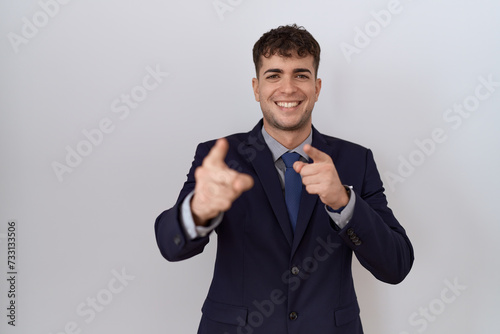 Young hispanic business man wearing suit and tie pointing fingers to camera with happy and funny face. good energy and vibes.