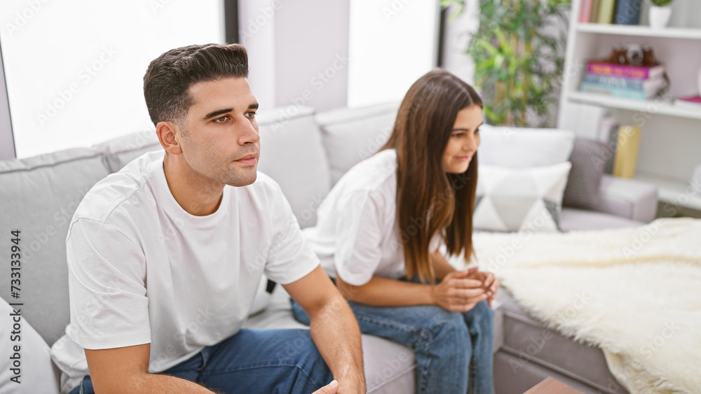 A contemplative couple sits apart on a sofa in their modern living room, depicting potential relationship issues. A contemplative couple sits apart on a sofa in their modern living room, depicting potential relationship issues.