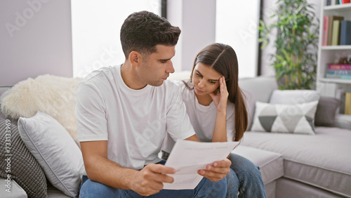 A concerned man and woman review a document together in their modern living room, reflecting on an important matter.