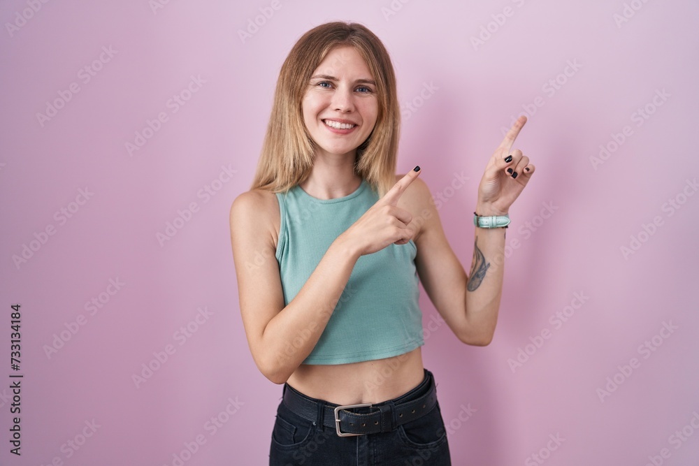 Blonde caucasian woman standing over pink background smiling and looking at the camera pointing with two hands and fingers to the side. Blonde caucasian woman standing over pink background smiling and looking at the camera pointing with two hands and fingers to the side.