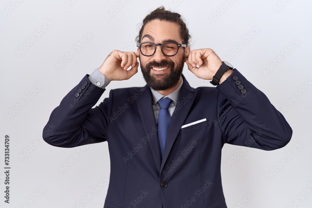 Hispanic man with beard wearing suit and tie covering ears with fingers with annoyed expression for the noise of loud music. deaf concept. Hispanic man with beard wearing suit and tie covering ears with fingers with annoyed expression for the noise of loud music. deaf concept.