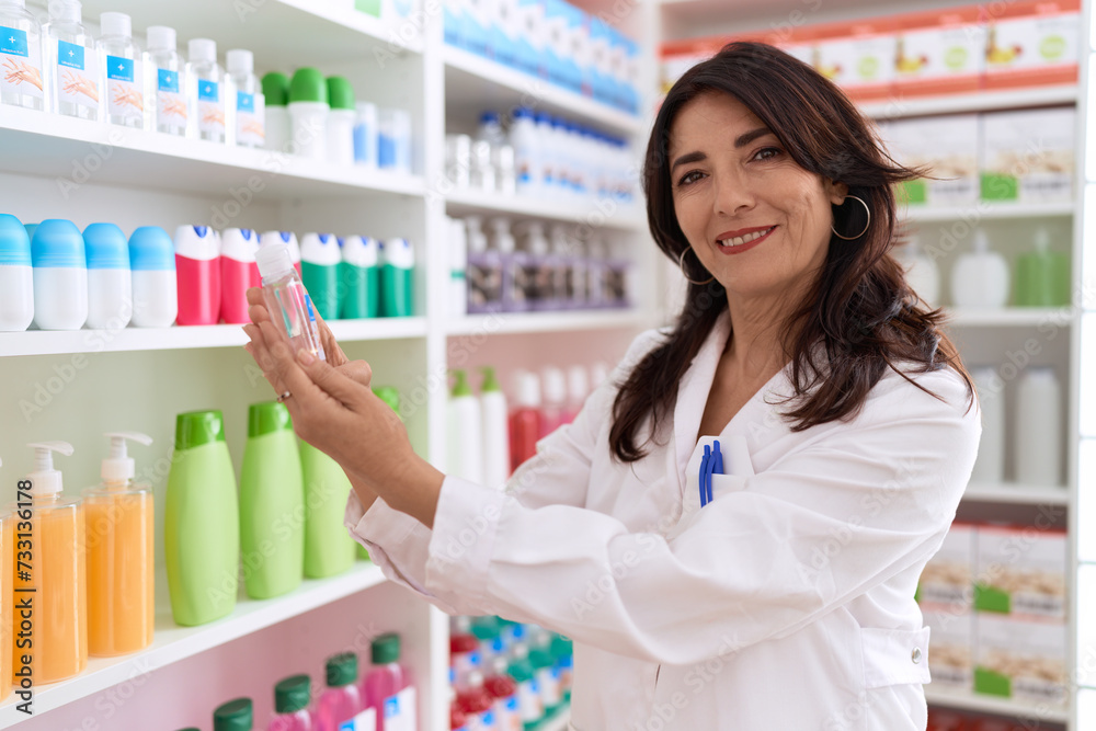Middle age hispanic woman pharmacist holding lotion bottle at pharmacy