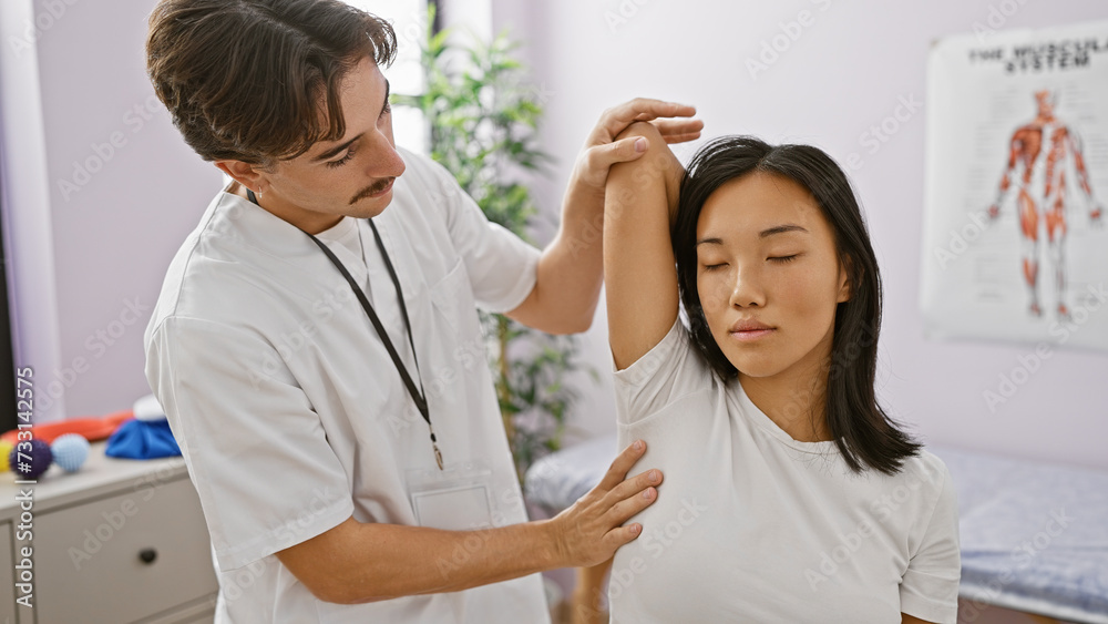 In a rehab clinic, a male physiotherapist assists a female patient, demonstrating shoulder exercises indoors.