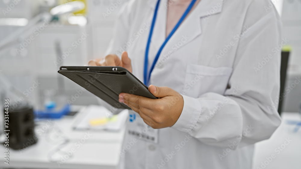 Hispanic woman in lab coat using tablet in laboratory setting Hispanic woman in lab coat using tablet in laboratory setting