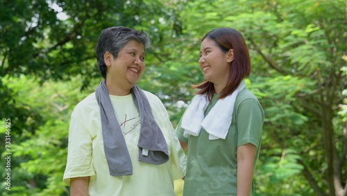 Attractive Senior mother and daughter working out together in the morning exercise in the park. Daughter absorbs sweat from her mom with white towel, a senior caregiver, and a happy family concept.