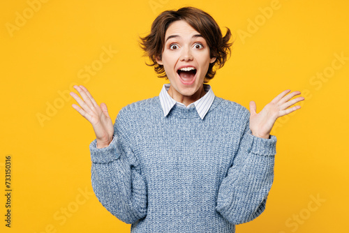 Young shocked surprised excited cool fun woman she wearing grey knitted sweater shirt casual clothes looking camera spread hands isolated on plain yellow background studio portrait. Lifestyle concept.