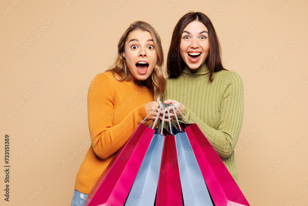 Young surprised shocked friends two women they wear orange green shirt casual clothes hold shopping paper package bags look camera isolated on plain beige background Black Friday sale buy day concept Young surprised shocked friends two women they wear orange green shirt casual clothes hold shopping paper package bags look camera isolated on plain beige background Black Friday sale buy day concept