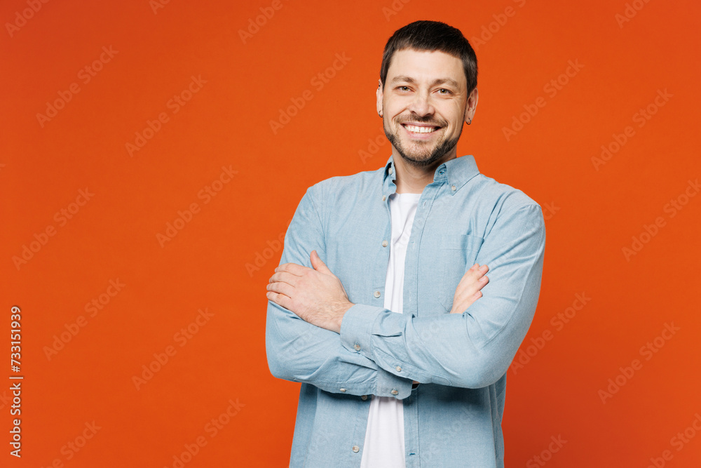 Young smiling happy cheerful man he wears blue shirt white t-shirt casual clothes looking camera hold hands crossed folded isolated on plain red orange background studio portrait. Lifestyle concept. Young smiling happy cheerful man he wears blue shirt white t-shirt casual clothes looking camera hold hands crossed folded isolated on plain red orange background studio portrait. Lifestyle concept.
