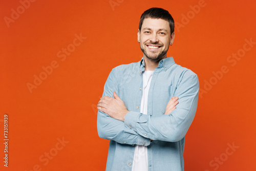 Young smiling happy cheerful man he wears blue shirt white t-shirt casual clothes looking camera hold hands crossed folded isolated on plain red orange background studio portrait. Lifestyle concept.