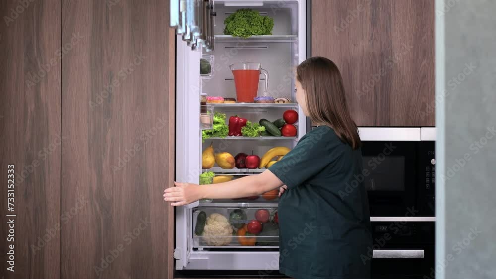Young pregnant woman takes an apple from the refrigerator at home. Young pregnant woman takes an apple from the refrigerator at home.