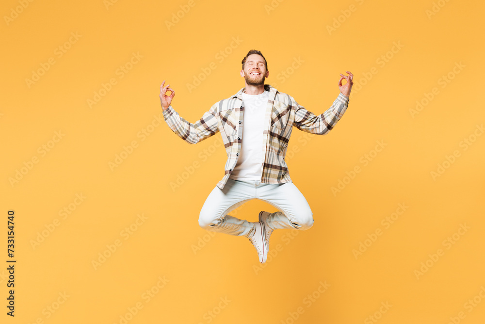 Full body spiritual young Caucasian man in brown shirt casual clothes jump high hold spreading hands in yoga om aum gesture relax meditate try to calm down isolated on plain yellow orange background