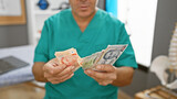 A middle-aged man in scrubs counts singapore dollars in a medical clinic's interior.