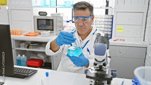 A mature male scientist examining a chemical in a flask within a modern laboratory setting.