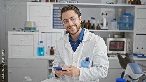 Young hispanic man scientist smiling confident using smartphone at laboratory