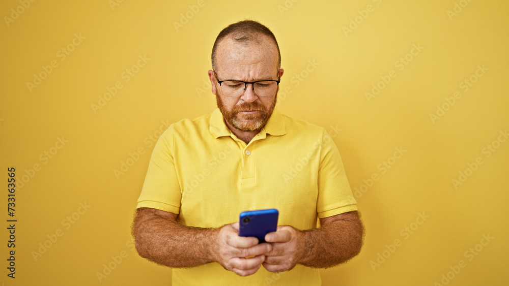 Caucasian man using smartphone with serious expression over isolated yellow background Caucasian man using smartphone with serious expression over isolated yellow background