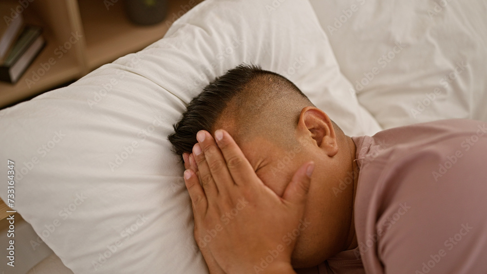 Handsome, young latin man stressfully crying, lying on his bed in a bedroom, plagued with insomnia, worried and unhappy Handsome, young latin man stressfully crying, lying on his bed in a bedroom, plagued with insomnia, worried and unhappy