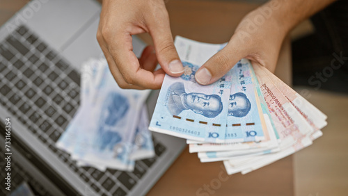 Fotografía Young adult sitting on his living room sofa counting yuan banknotes, managing hi