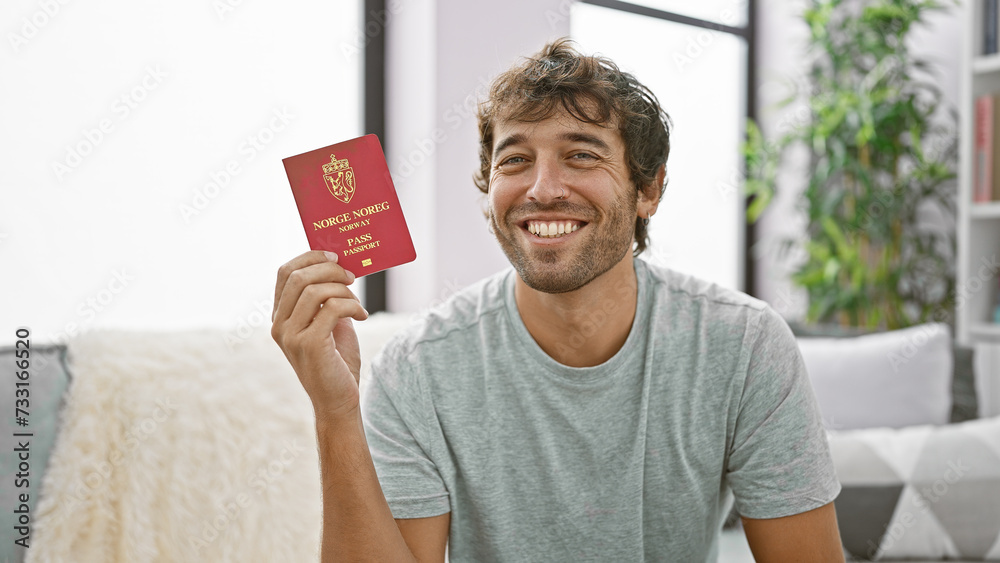 Joyful young man chilling on the sofa, casually holding his norway passport and beaming with confidence at home Joyful young man chilling on the sofa, casually holding his norway passport and beaming with confidence at home
